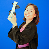 Ivy Tong stands in front of blue wall holding VR headset, smiling to camera